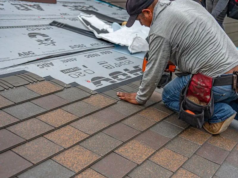 Installer fastening architectural shingles during a full roof replacement