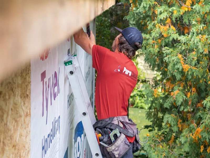 Contractor on a ladder working on a home's exterior wall before new siding