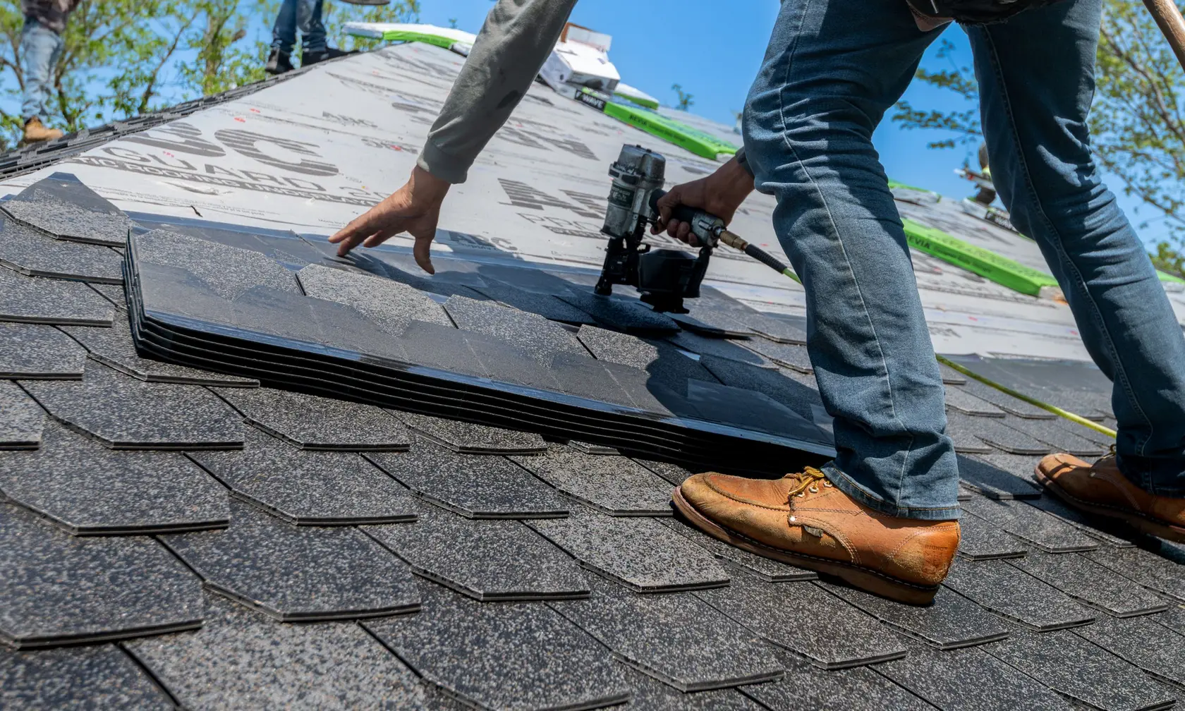Roofer securing asphalt shingles with a nail gun on a residential roof